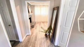 Un couloir avec un plancher en bois, des murs blancs et une porte sur le côté droit.