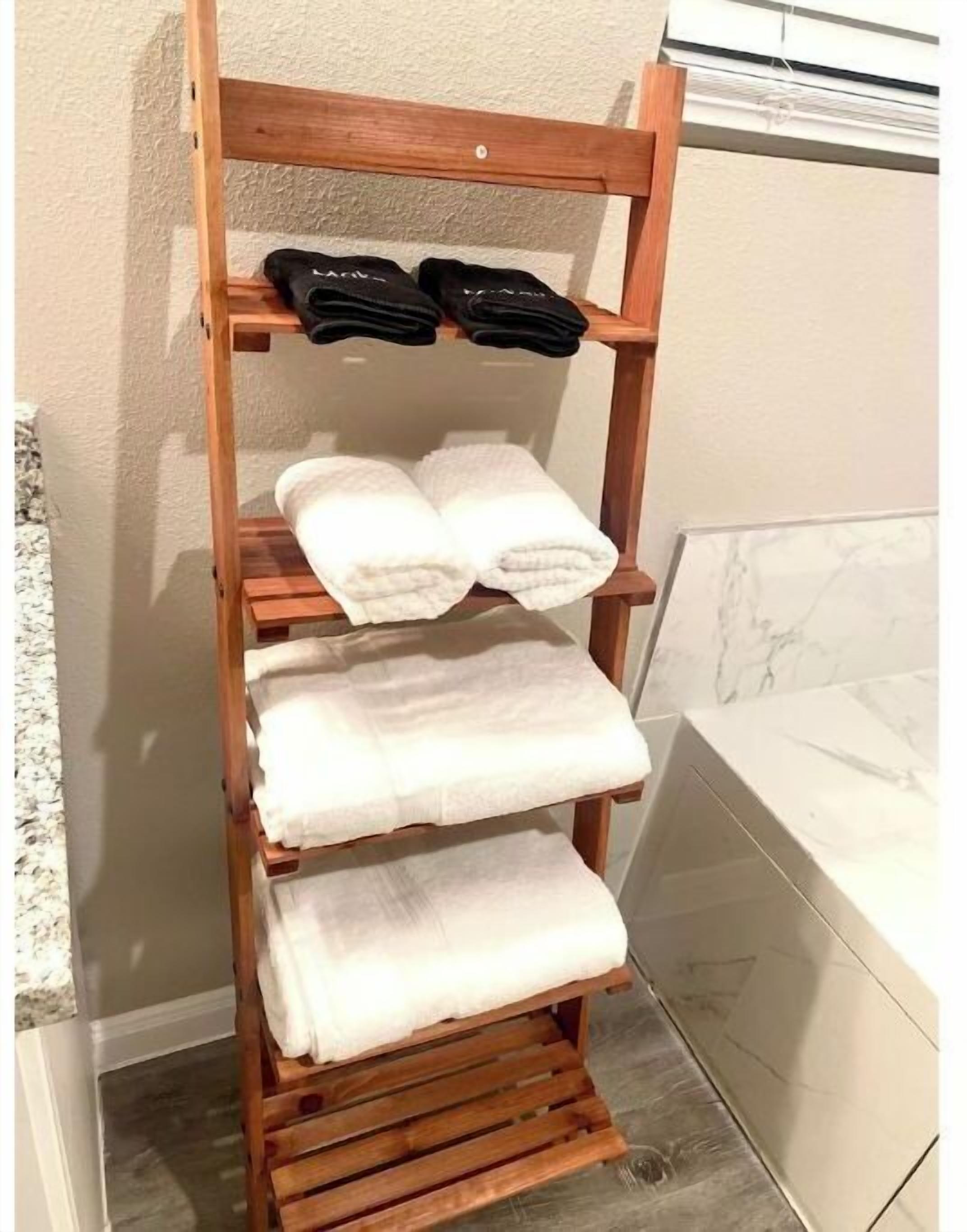 Ett trähandduksställ med tre vita handdukar och två svarta tofflor.