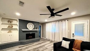 Un salon moderne avec une cheminée, un canapé noir et un ventilateur de plafond.