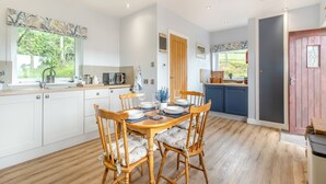 Een moderne keuken met witte kasten, een houten eettafel met vier stoelen en uitzicht op de tuin door het raam.