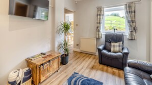 Een moderne woonkamer met een leren bank, een houten salontafel, een televisie en uitzicht op een groen landschap door een raam.