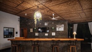 A bar area with a wooden counter, three stools, a television, and a ceiling fan. - Santorini Village - Hotel Boutique (Tamanique)