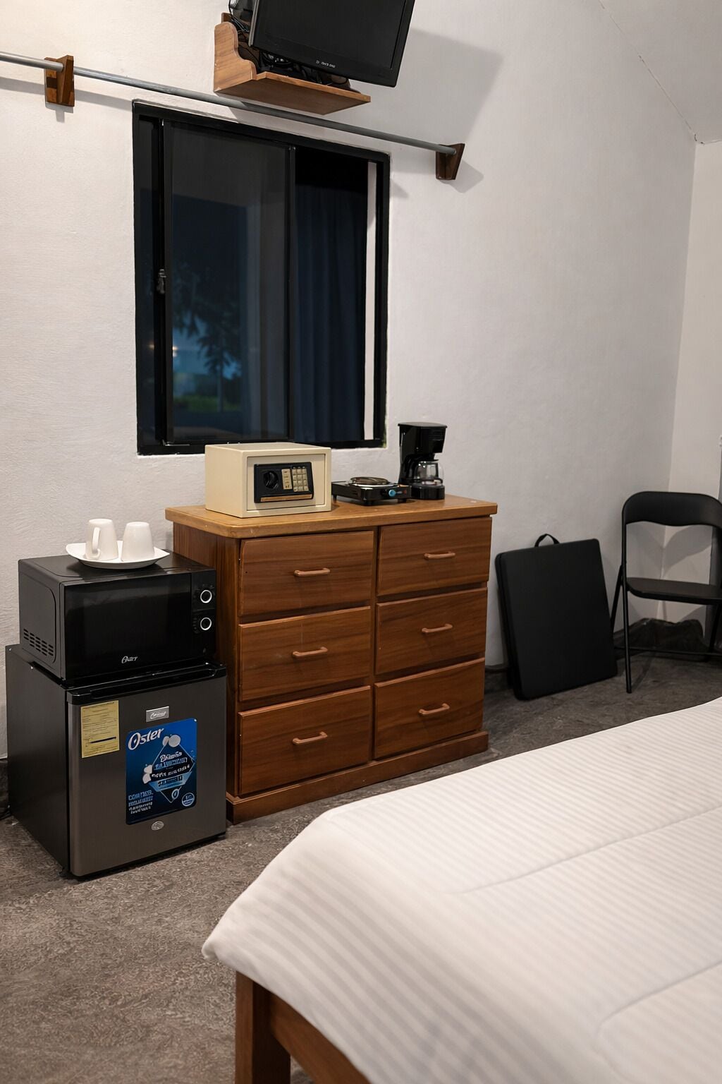 A hotel room with a bed, a wooden dresser, a coffee maker, a microwave, and a television mounted on the wall.