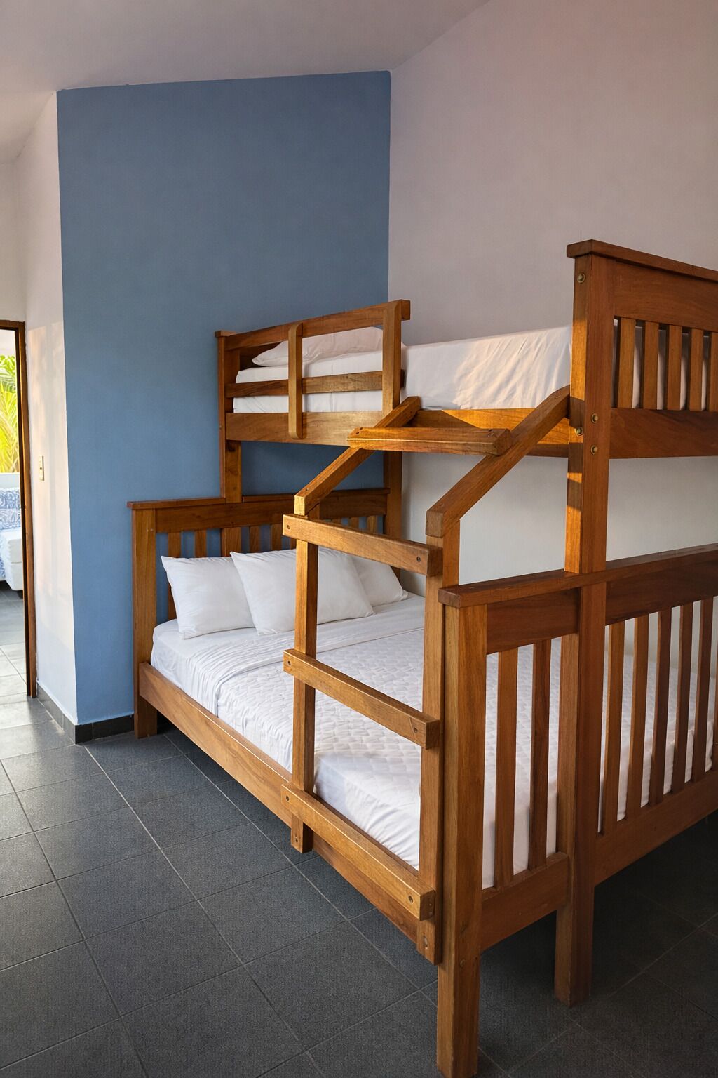 A bunk bed with a wooden frame and white bedding in a room with blue walls and tiled flooring.