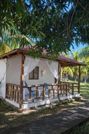 A small, rustic-style building with a wooden porch and white curtains. - Santorini Village - Hotel Boutique (Tamanique)