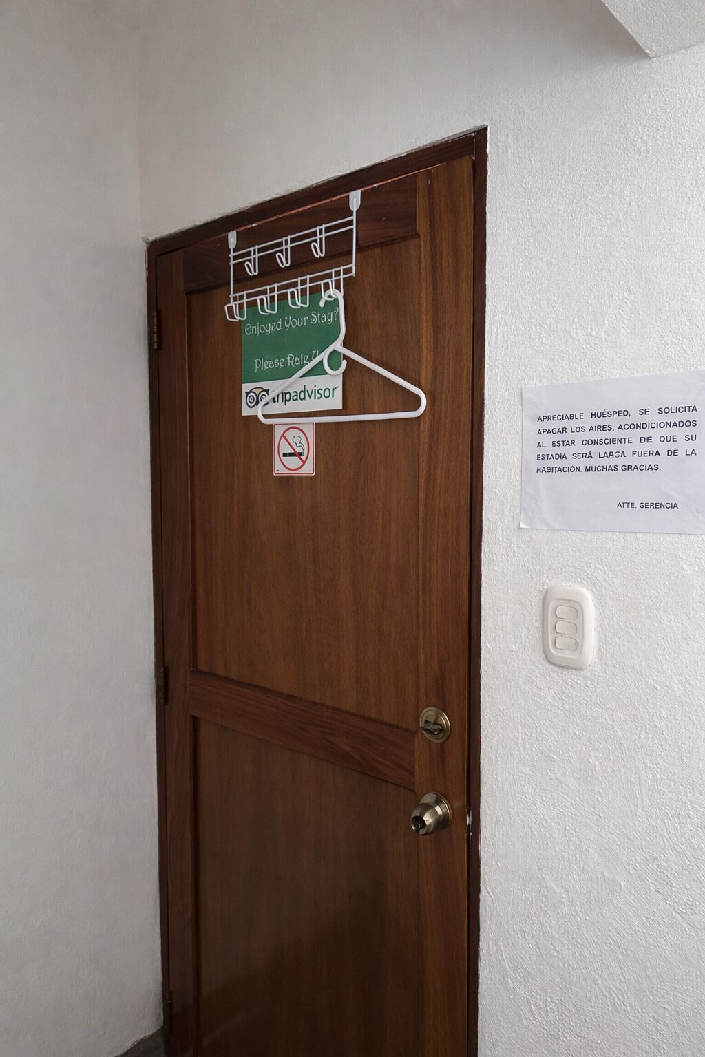 Uma porta de madeira com uma placa pedindo aos hóspedes que avaliem a estadia e um aviso de proibição de fumar.