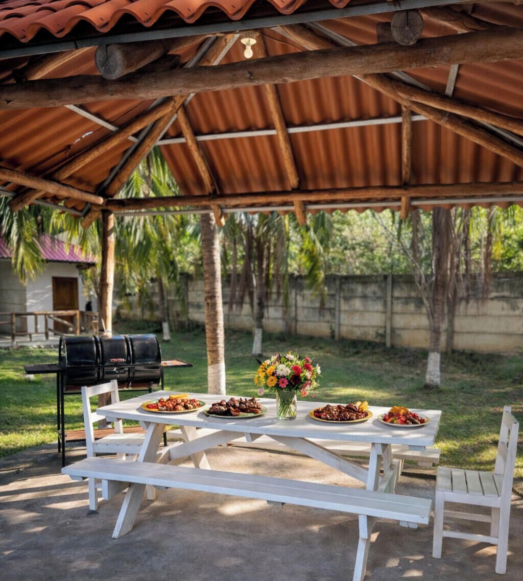 An outdoor dining area with a covered pavilion, a grill, and a table set with food and a floral centerpiece.