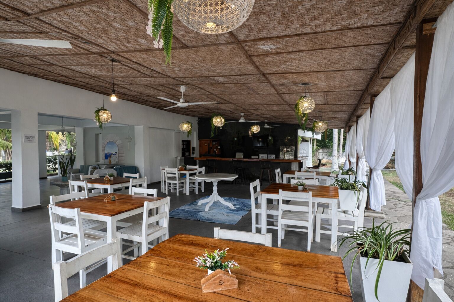 Ein Restaurant mit Holztischen und weißen Stühlen, einer Bar und hängenden Lampen.