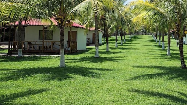 A row of bungalow-style accommodations with red roofs, surrounded by well-maintained grass and palm trees. - Santorini Village - Hotel Boutique (Tamanique)