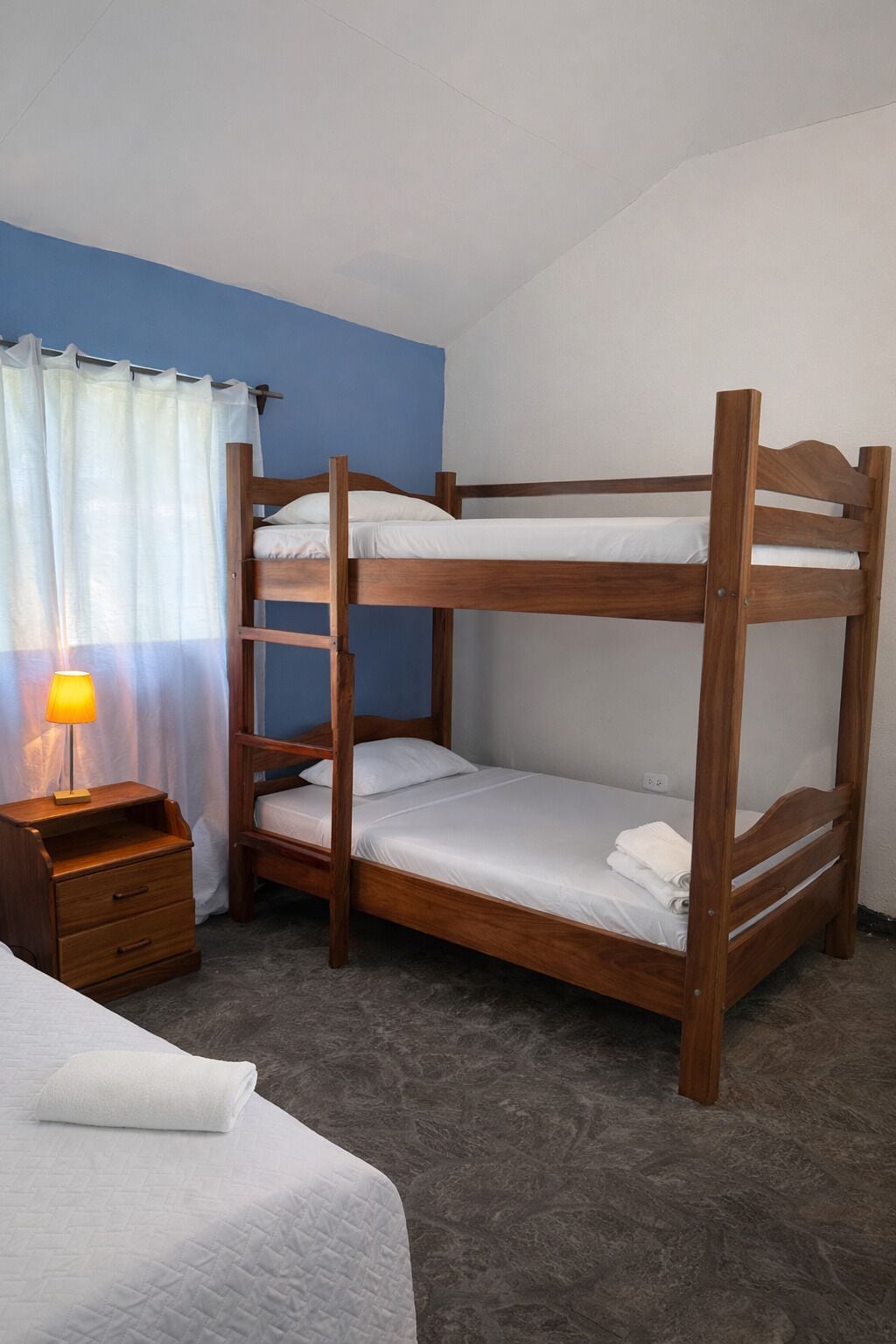 A bunk bed with a wooden frame, a bedside table with a lamp, and a white bedspread.