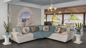 A modern living room with a sectional sofa, a decorative archway, and a dining area with outdoor seating. - Santorini Village - Hotel Boutique (Tamanique)