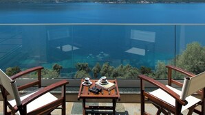 A balcony with two wooden chairs and a table, overlooking a clear blue lake and mountains. - Stylish Contemporary Villa with Sea Views and Steps to the Water (Meganissi)