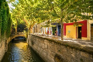 Un estrecho canal con un puente de piedra, bordeado por árboles y edificios de fachadas coloridas.