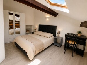 A bedroom with a bed, bedside tables, a desk, a chair, a wardrobe, and a skylight.