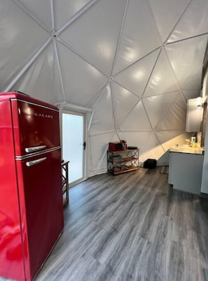Una cucina compatta e moderna, con un frigorifero rosso, un soffitto bianco decorato con motivi geometrici e un piano di lavoro grigio.