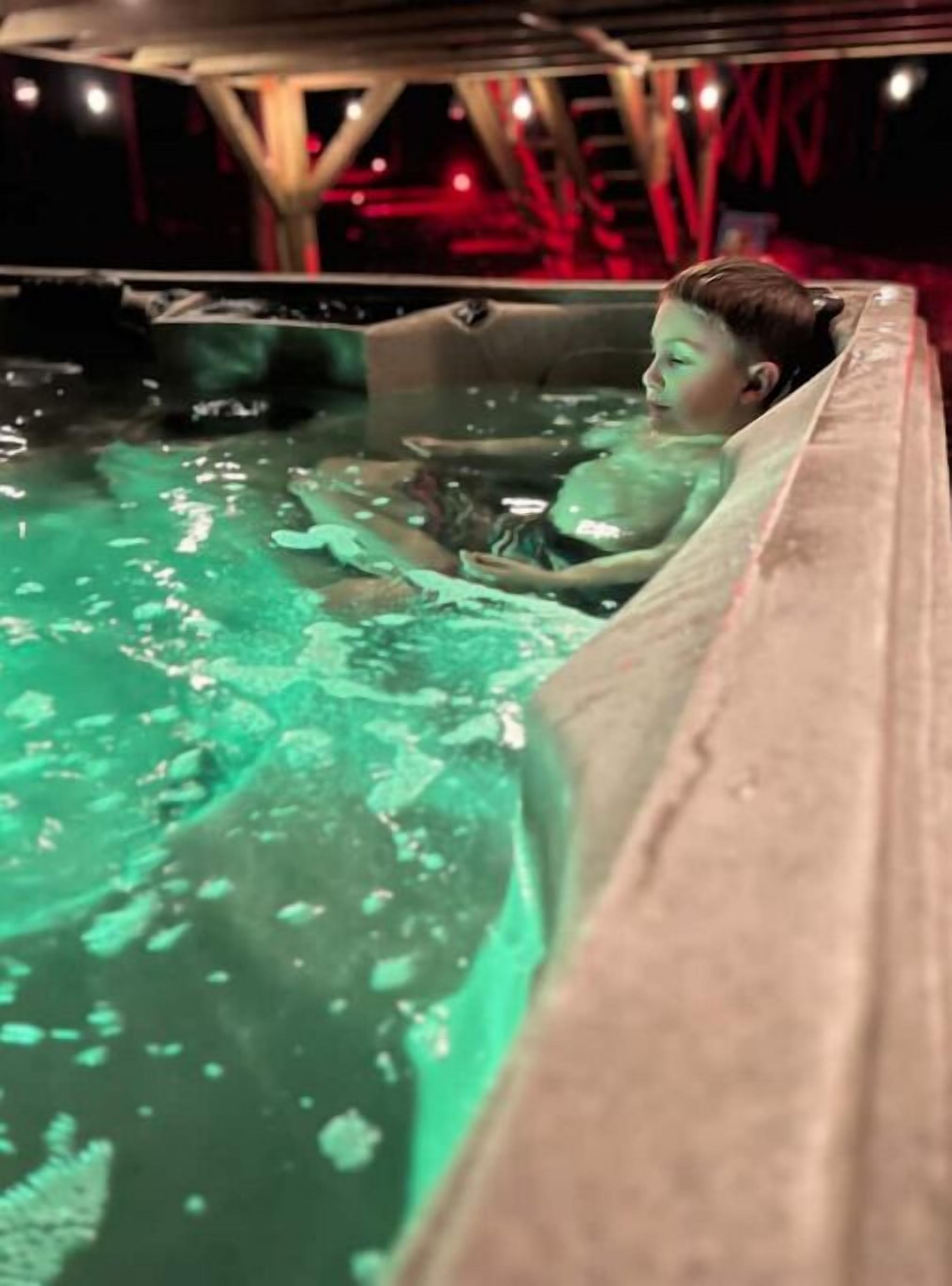 Niño en un jacuzzi con un tono verdoso, rodeado por una estructura con iluminación roja.