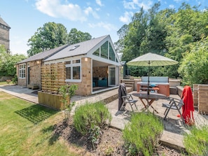 Une maison en pierre avec un patio, un espace barbecue et une clôture en bois.