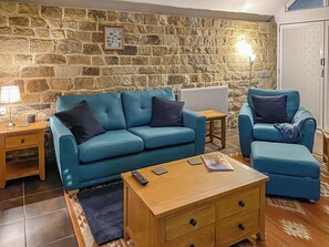 A living room with a stone wall, a blue sofa, a matching armchair, a wooden coffee table, and a lamp. - Church Cottage nestles in the grounds of the Old Vicarage in Darley Bridge. (Darley Bridge, near Matlock)