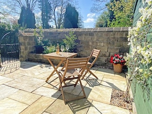 Une terrasse avec une table en pierre et des chaises en bois, un mur en pierre et un portail.