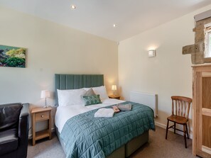 A bedroom with a bed, a chair, a nightstand, a radiator, and a wall-mounted light fixture. - Church Cottage nestles in the grounds of the Old Vicarage in Darley Bridge. (Darley Bridge, near Matlock)