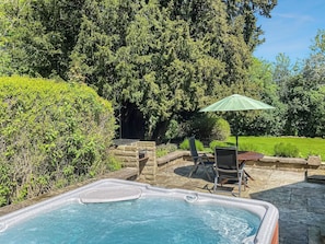 Un bain à remous entouré de pierres, une table de patio avec des chaises et un parasol vert.