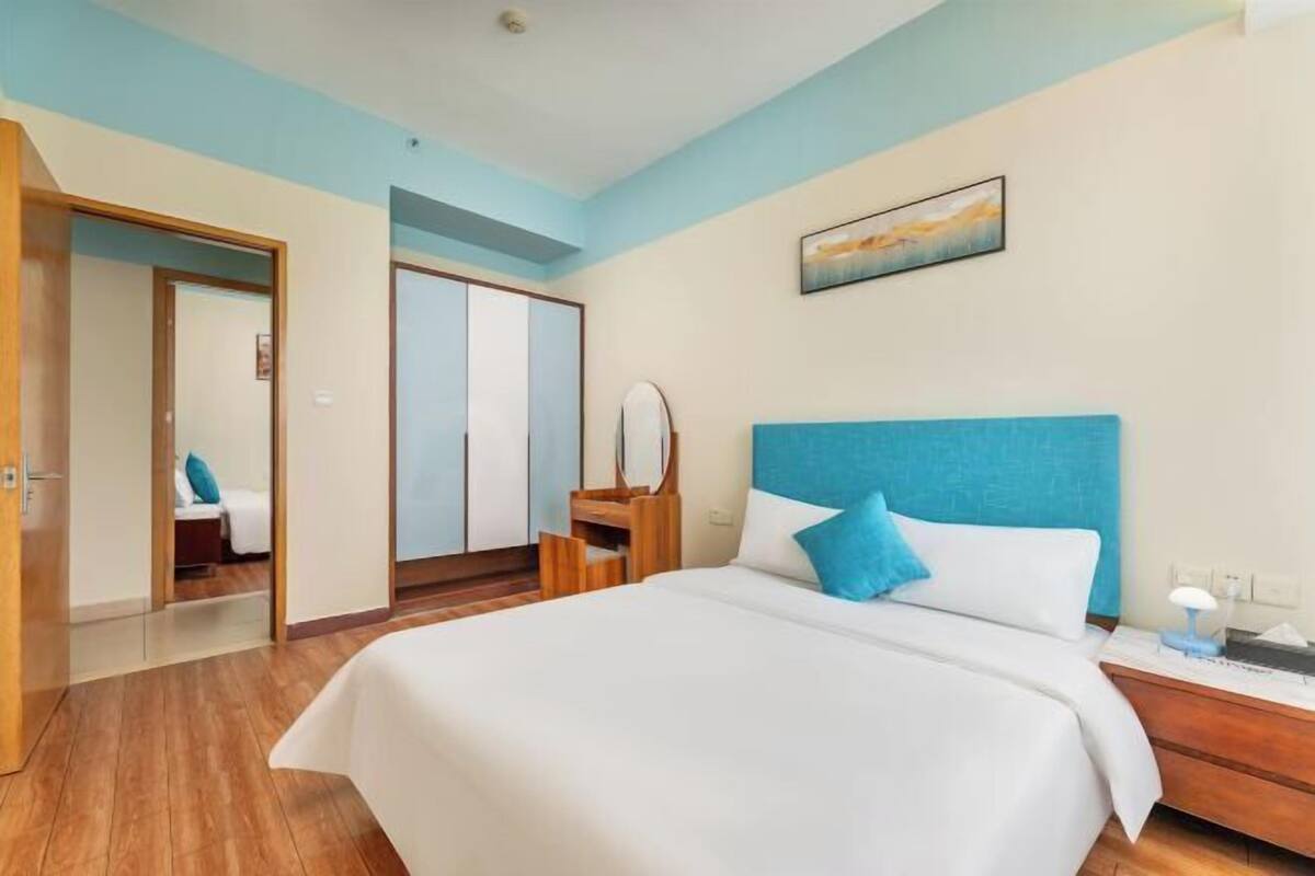 Une chambre d’hôtel avec un grand lit, un plancher en bois, une tête de lit bleue et un tableau accroché au mur.
