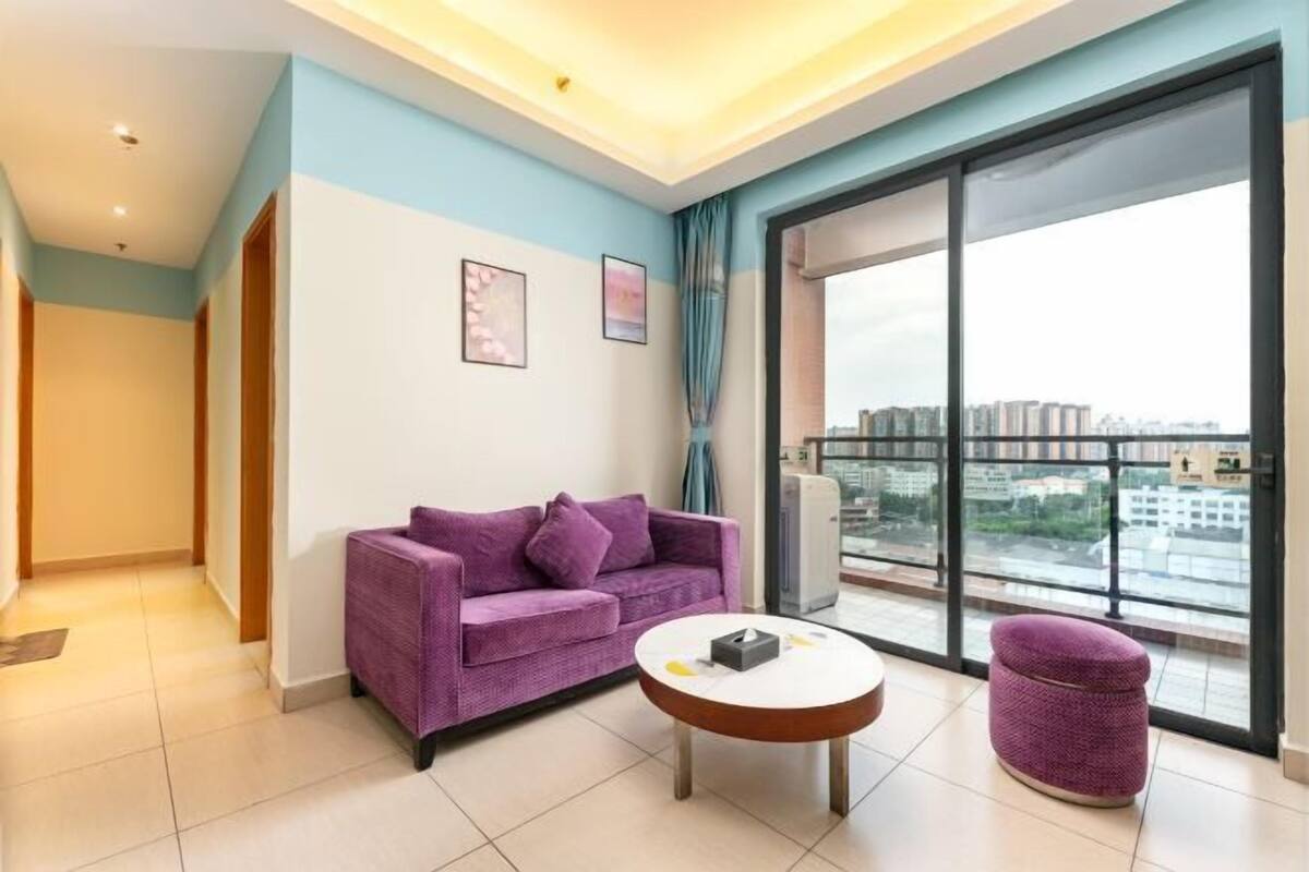 Un salon moderne avec un canapé violet, une table basse ronde et une vue sur le paysage urbain à travers de grandes fenêtres.