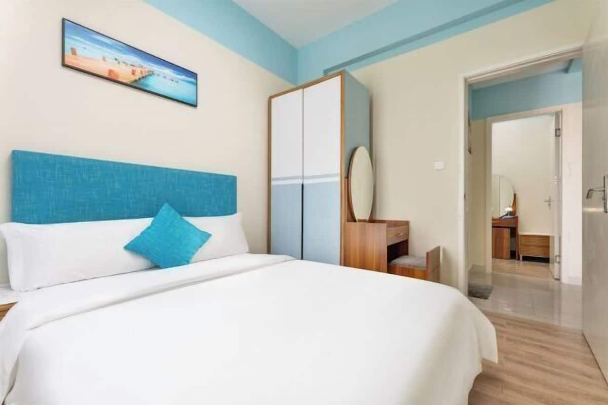 Une chambre d’hôtel avec un lit, une armoire, un bureau et une salle de bain visible à travers une porte ouverte.
