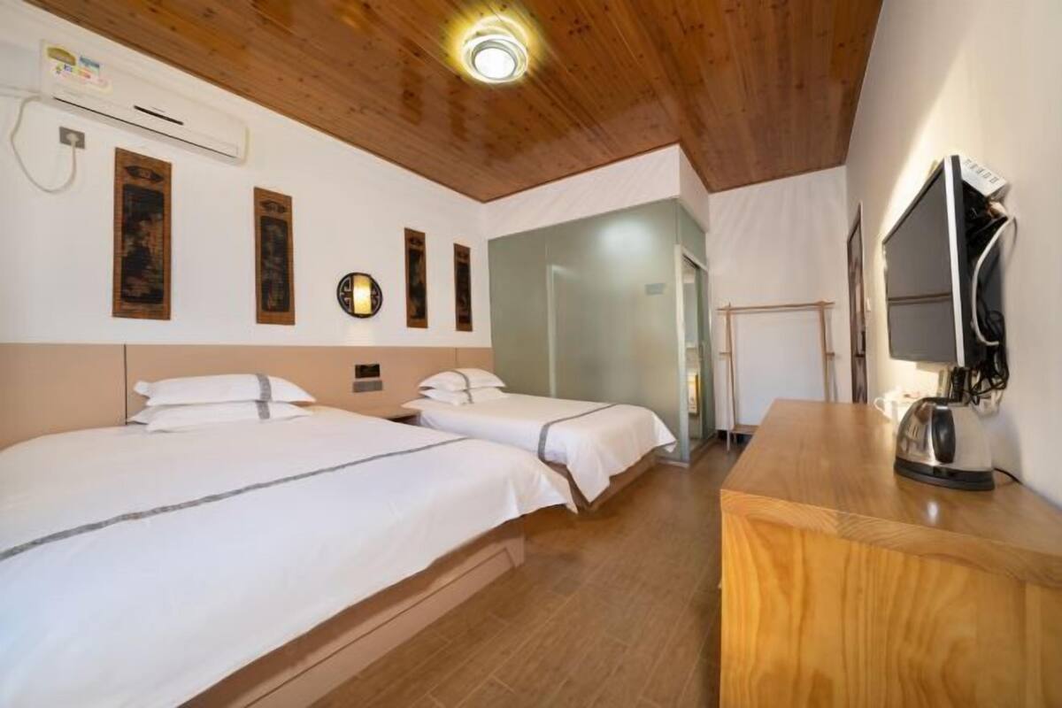 A hotel room with two beds, a wooden ceiling, a desk with a kettle, and a mirror.