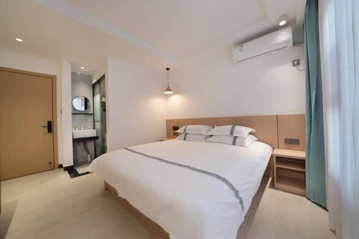 A hotel room with a bed, bedside table, a mirror, a sink, and an air conditioning unit.