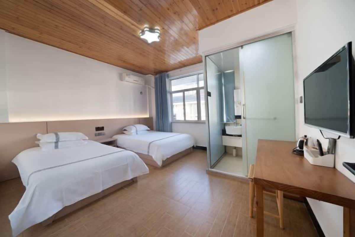 A hotel room with two beds, a wooden ceiling, a TV, and a desk.
