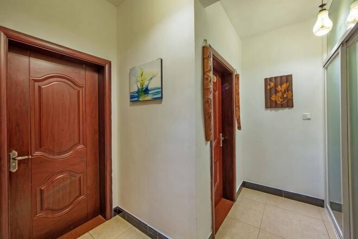 A hallway with wooden doors, a painting on the wall, and a light fixture.