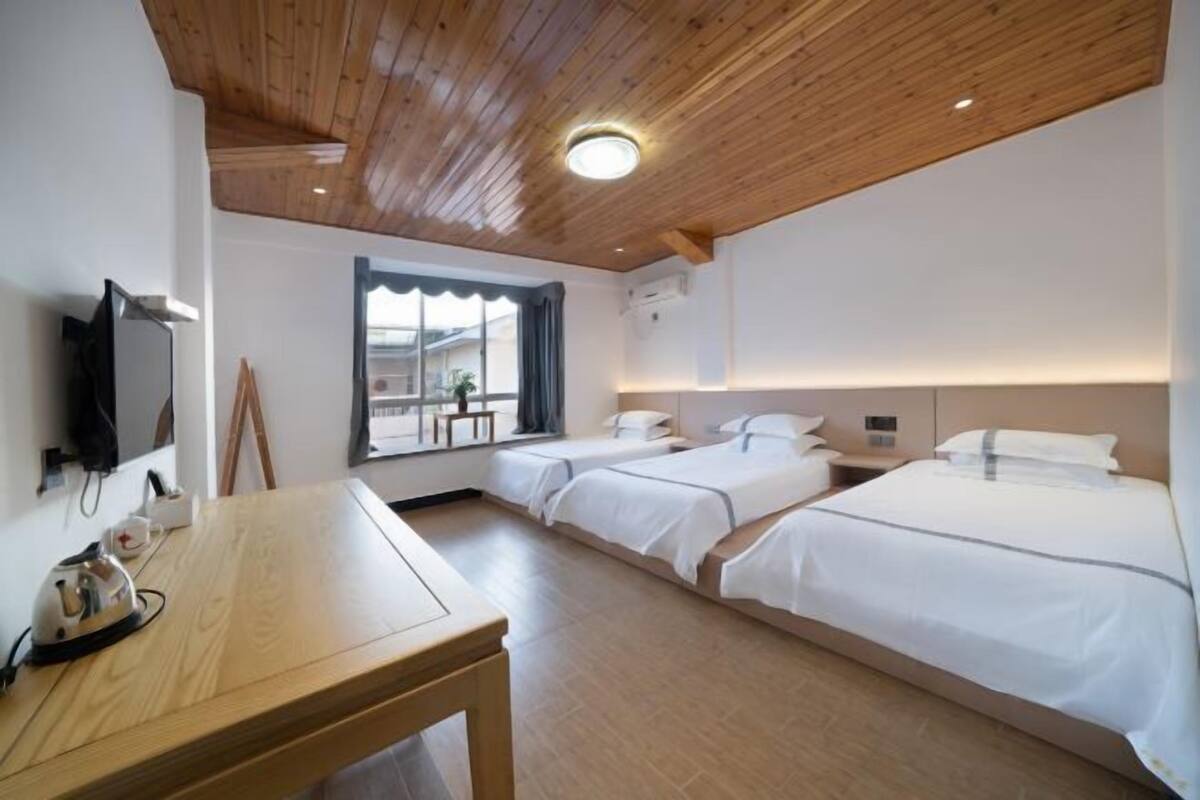 A hotel room with wooden ceiling, two beds, a TV, a table, and a window with curtains.