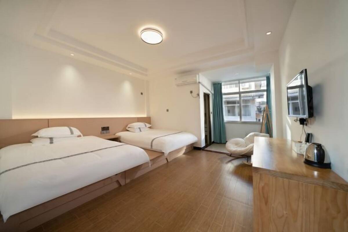 A hotel room with two beds, a wooden desk, a flat-screen TV, and a view of the city.