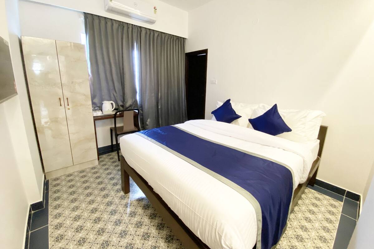A hotel room with a bed, a desk, an air conditioning unit, and a wardrobe.