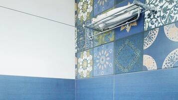Un baño con azulejos azules, un inodoro blanco, un lavabo, un perchero para toallas y un cabezal de ducha.