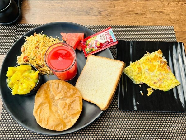 Une assiette contenant divers aliments, notamment une tranche de pain, un morceau d’omelette, un bol d’un plat jaune, une tranche de pastèque, un emballage de jus de fruits et un verre d’une boisson rouge.