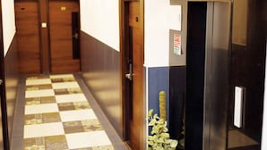 Un pasillo de hotel con piso a cuadros, puertas de madera y un ascensor con letrero que dice 'Lift'.