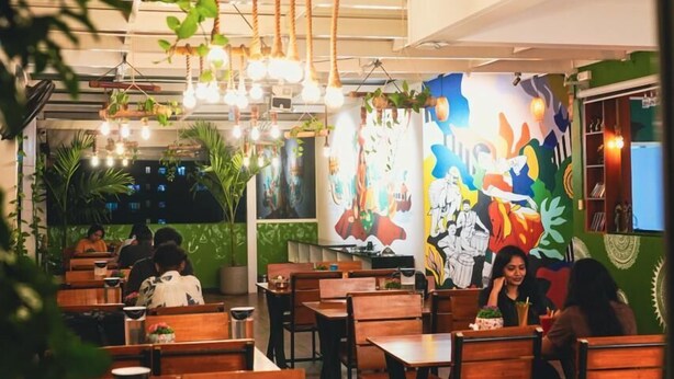 Un restaurante con mesas y sillas de madera, lámparas colgantes y un mural en la pared.