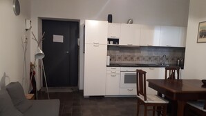 Une cuisine compacte avec des meubles blancs, un four encastré et un coin repas comprenant une table et des chaises en bois.