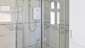 Een moderne badkamer met een douchecabine van glas, een handdouche en een bedieningspaneel.