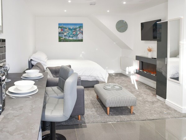 Une chambre d’hôtel moderne équipée d’un lit, d’un canapé, d’une table à manger avec de l’assiette, d’un tableau, d’une cheminée et d’un téléviseur.