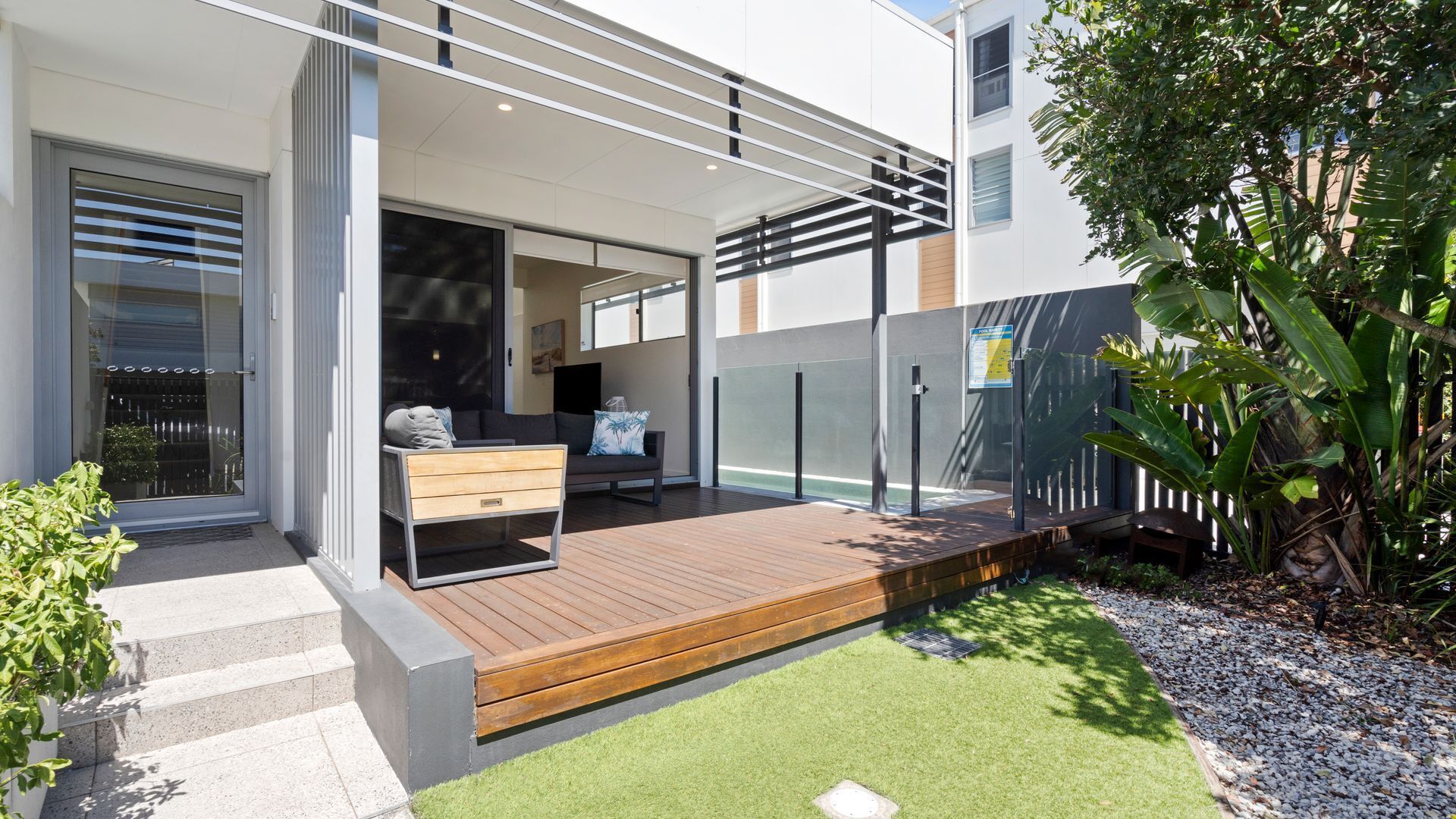 Un patio moderno al aire libre con piso de madera, un sofá y una mesita.