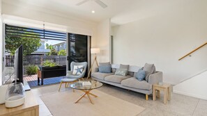 Un salon moderne avec un canapé gris, une table basse en verre et un fauteuil agrémenté d’un coussin en forme d’étoile de mer. Une grande fenêtre offre une vue sur l’extérieur.