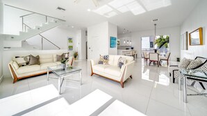 A modern living room with two white sofas, a glass coffee table, and a staircase leading to an upper level.