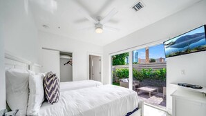 A modern bedroom with a large bed, a ceiling fan, and a TV mounted on the wall.