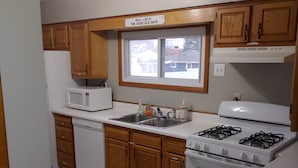 A kitchen with wooden cabinets, a microwave, a sink, a stove, and a window with a view of houses.