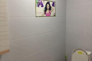 A bathroom with white tiled walls, a toilet with a yellow sign, and a poster with purple flowers. - Youpeng Holiday Hotel (Yangxin)