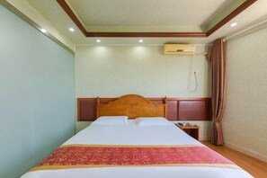 A hotel room with a large bed, a wooden headboard, a bedside table, and a wall-mounted air conditioning unit. - Youpeng Holiday Hotel (Yangxin)
