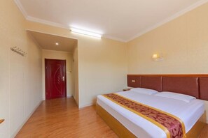 A hotel room with a wooden floor, a large bed with a patterned bedspread, a red door, and a wall-mounted light fixture. - Youpeng Holiday Hotel (Yangxin)